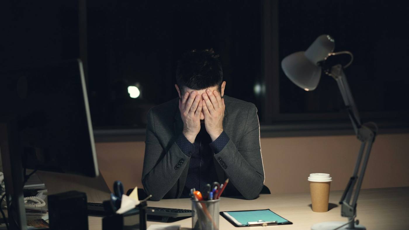 A business owner alone at his desk late at night, head in his hands
