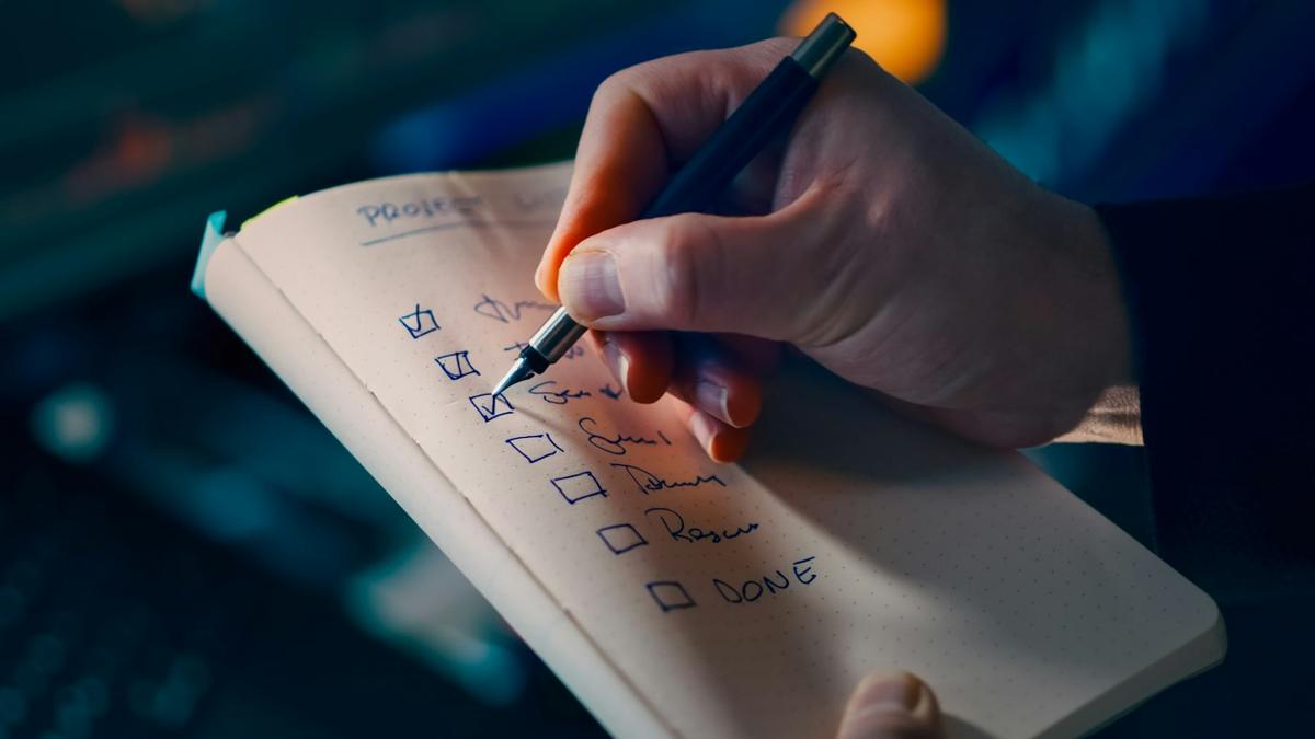 Close-up of hands writing in a notebook, a phone face-down on the table.